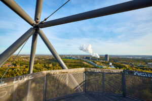 Tetraeder Halde Beckstr. Bottrop: Blick von Tetraeder Bottrop über das Ruhrgebiet, Schornsteine im Hintergrund, unter blauem Himmel.