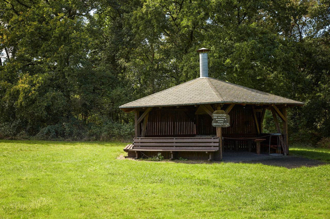 Waldkompetenzzentrum Heidhof Bottrop: Holzüberdachte Picknickhütte im Grünen mit Bänken, umgeben von Bäumen in Bottrop.