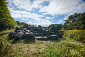 Waldkompetenzzentrum Heidhof Bottrop: ```html
Große dunkle Steine bilden einen natürlichen Felsenhügel unter einem blau-weißen Himmel.
```