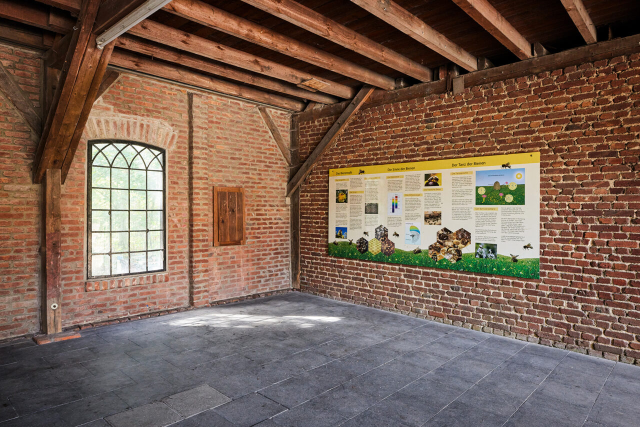 Waldkompetenzzentrum Heidhof Bottrop: Innenansicht eines Ziegelsteinraums mit hölzerner Dachkonstruktion und Info-Tafel an der Wand.