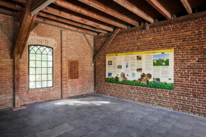 Waldkompetenzzentrum Heidhof Bottrop: Innenansicht eines Ziegelsteinraums mit hölzerner Dachkonstruktion und Info-Tafel an der Wand.