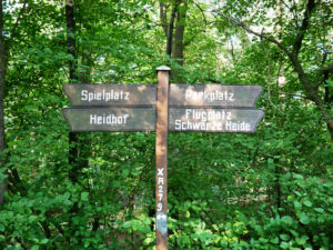 Waldkompetenzzentrum Heidhof, Bottrop, Wegweiser: Holzwegweiser im Wald mit Schildern zu Spielplatz, Heidhof, Parkplatz und Flugplatz Schwarze Heide